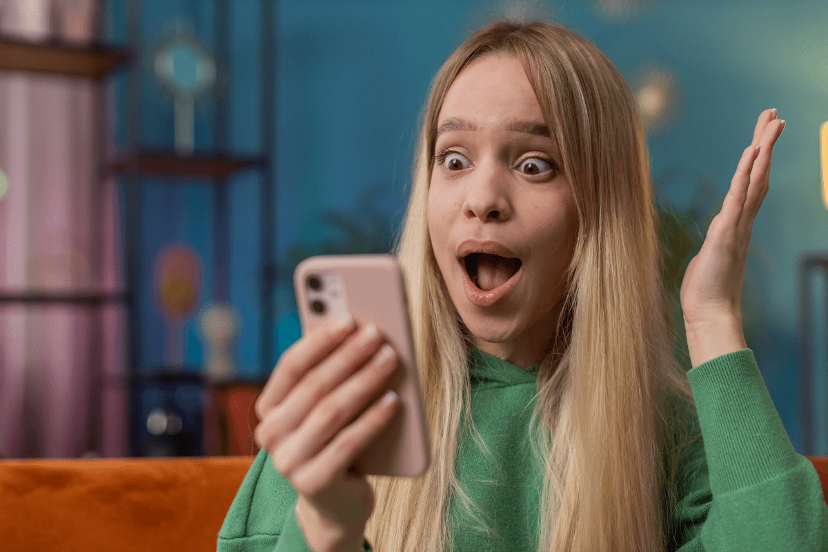 mulher olhando para o celular com alegria e espanto